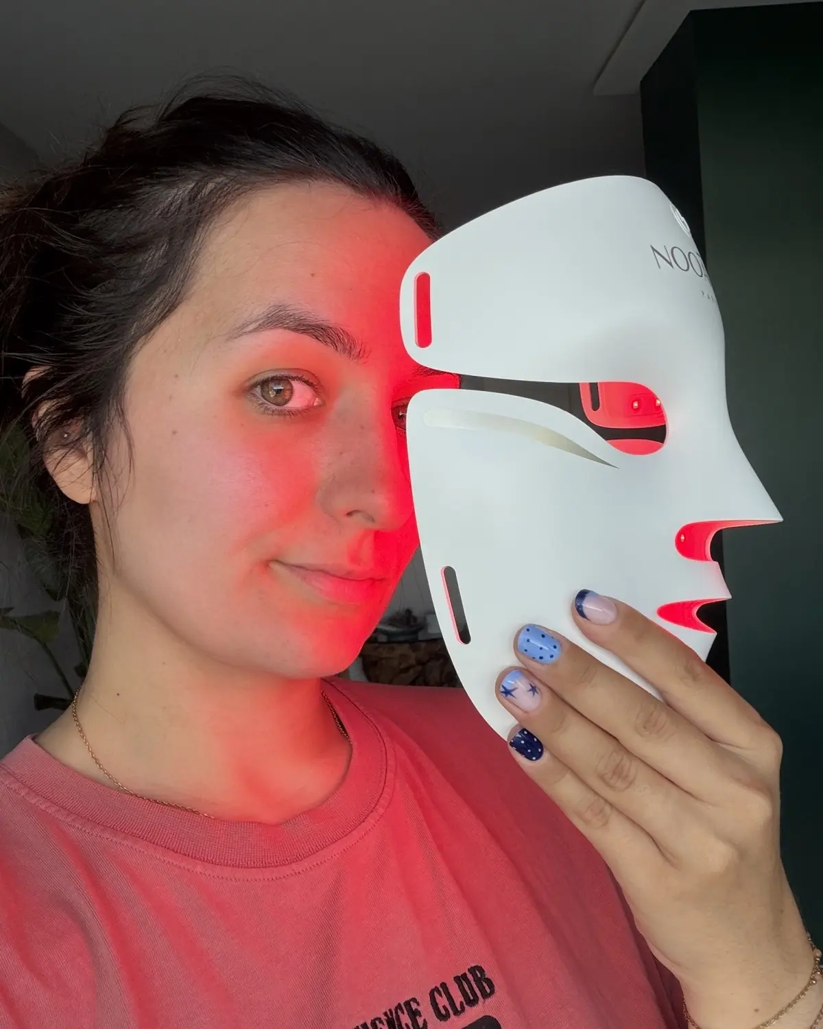 Emilie holding a lit LED mask beside her face, red light falling on her skin