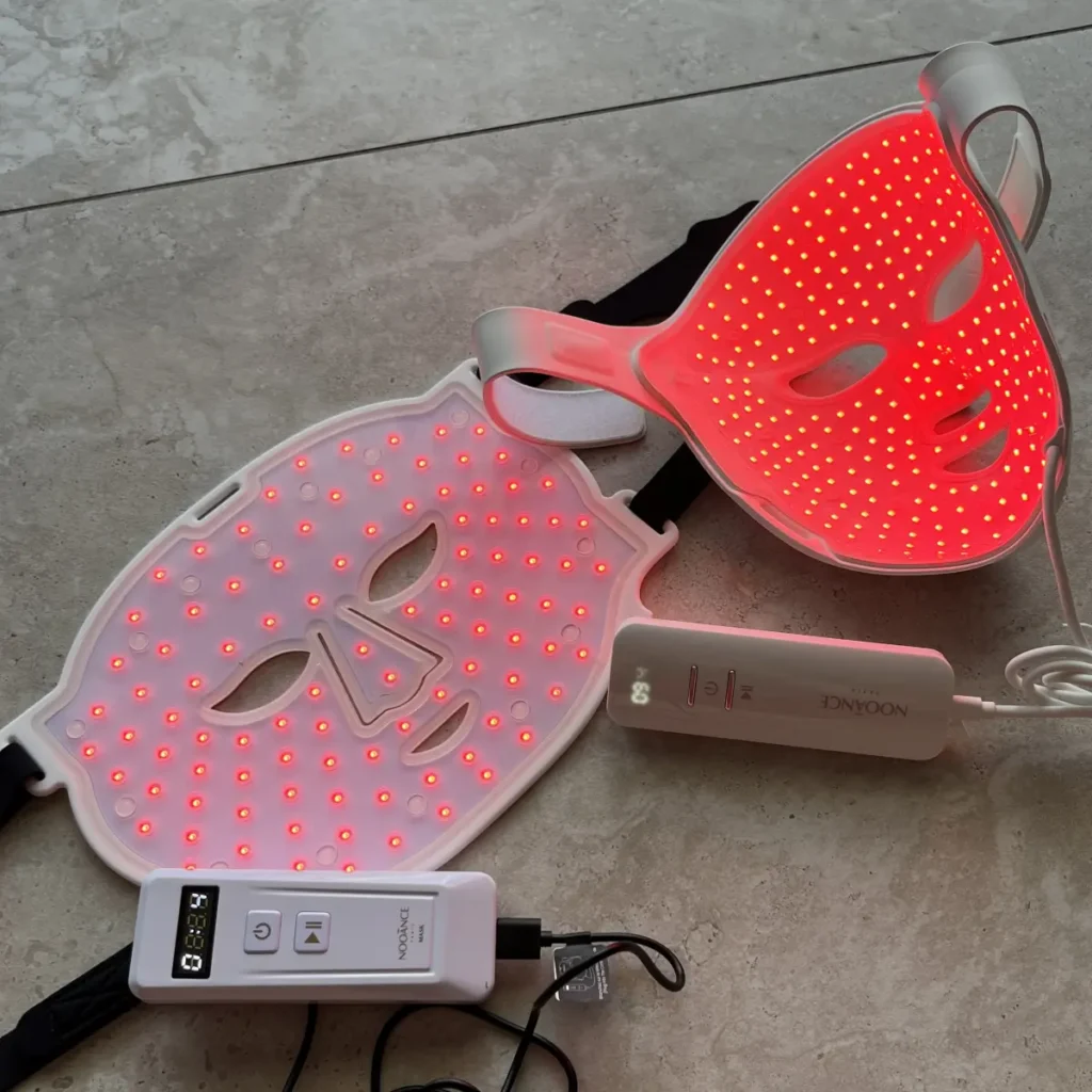 Two LED masks from the same brand lying side by side with their controllers, both lit red, carrying different numbers of diodes over the same face area