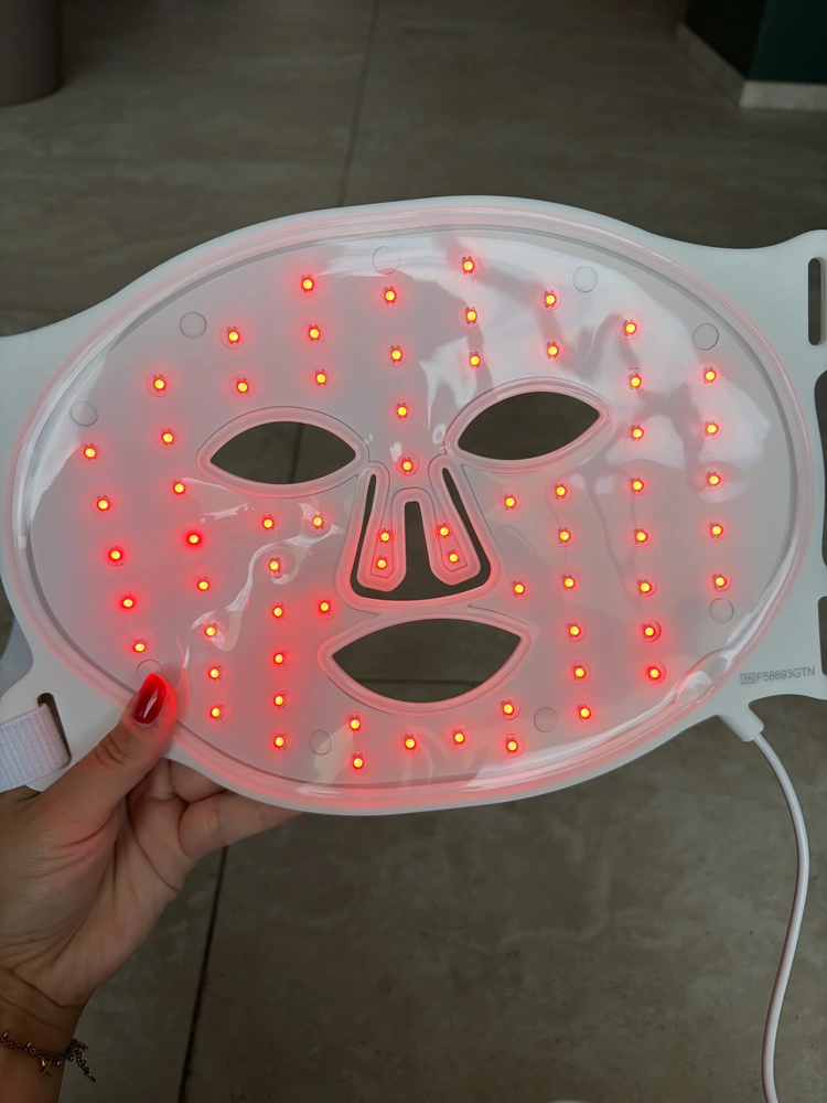The Omnilux Contour Face LED mask lit in a dark room, showing 66 separate points of light
