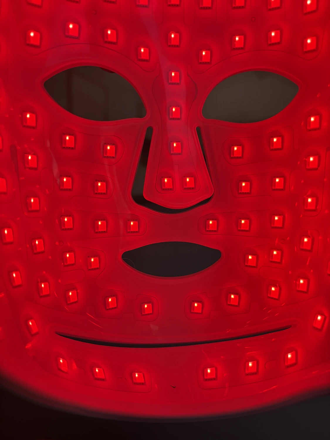 Straight-on close-up of the lit CurrentBody Series 2 mask, showing the bare cutouts at the eyes, nose and mouth and the spacing between diodes