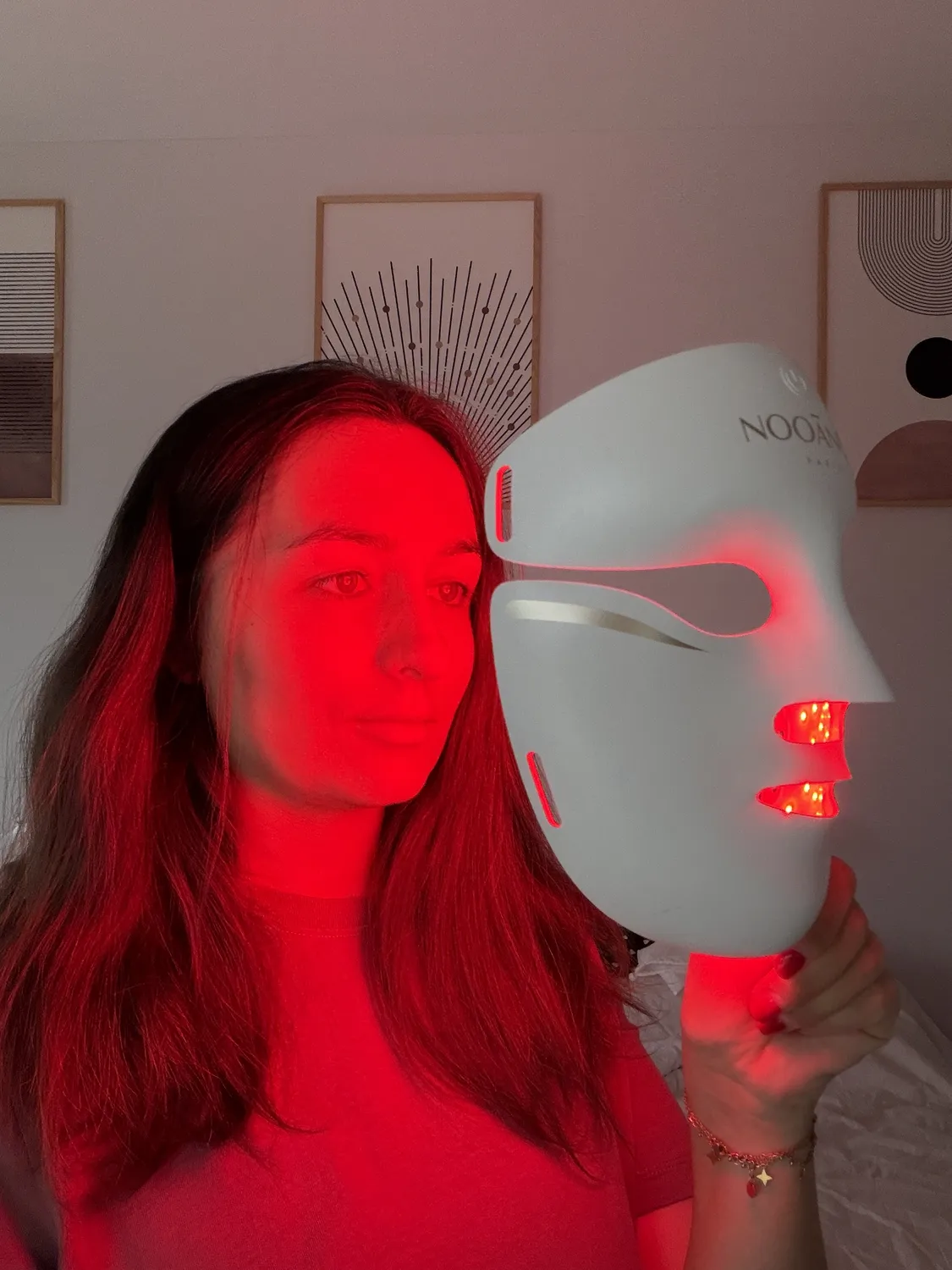 Emilie holding the lit Aurion X252 LED mask a few inches from her face, red light on her cheek