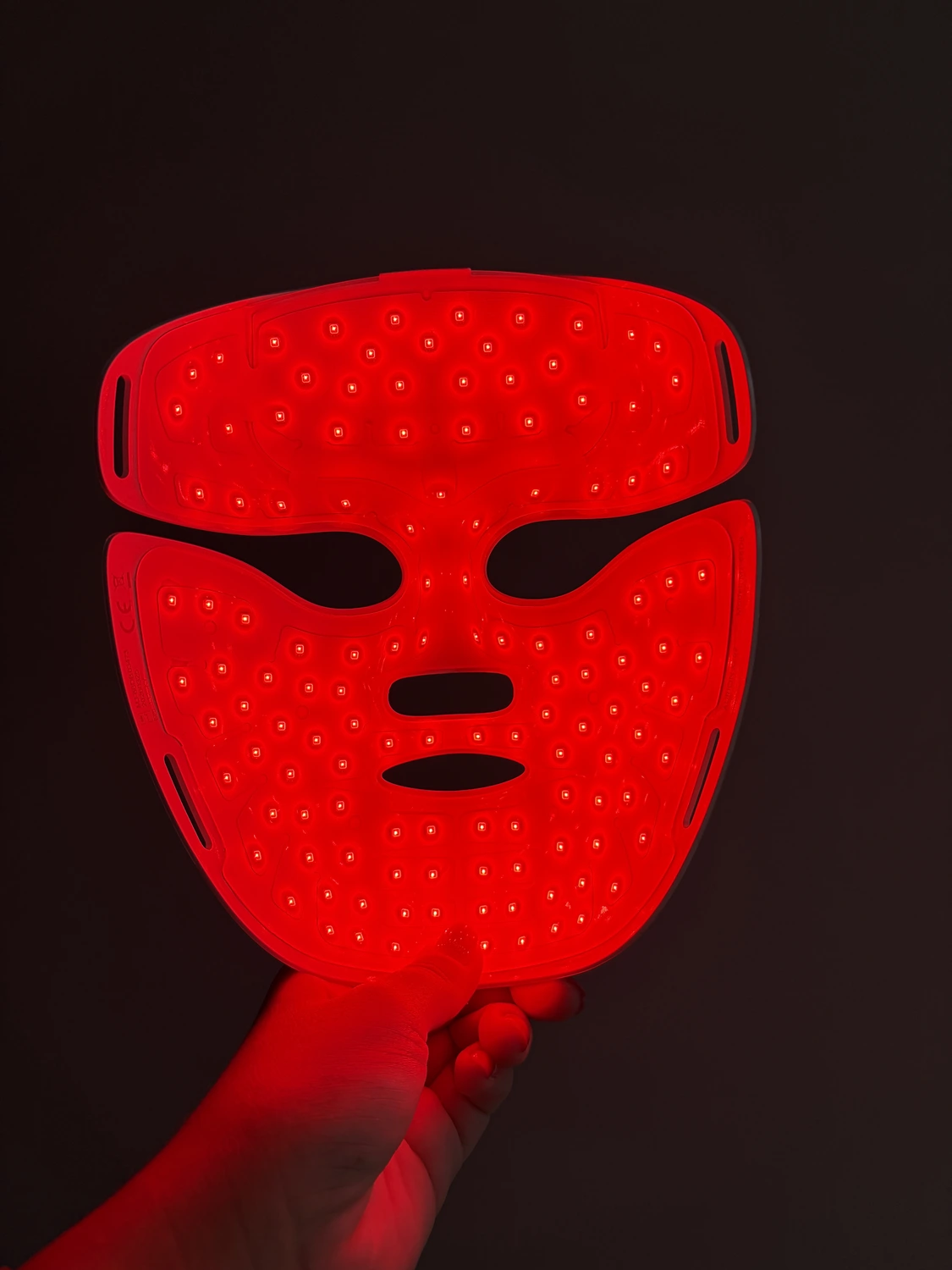 Inside of the lit Aurion X252 LED mask held in one hand, showing every light point on the red silicone
