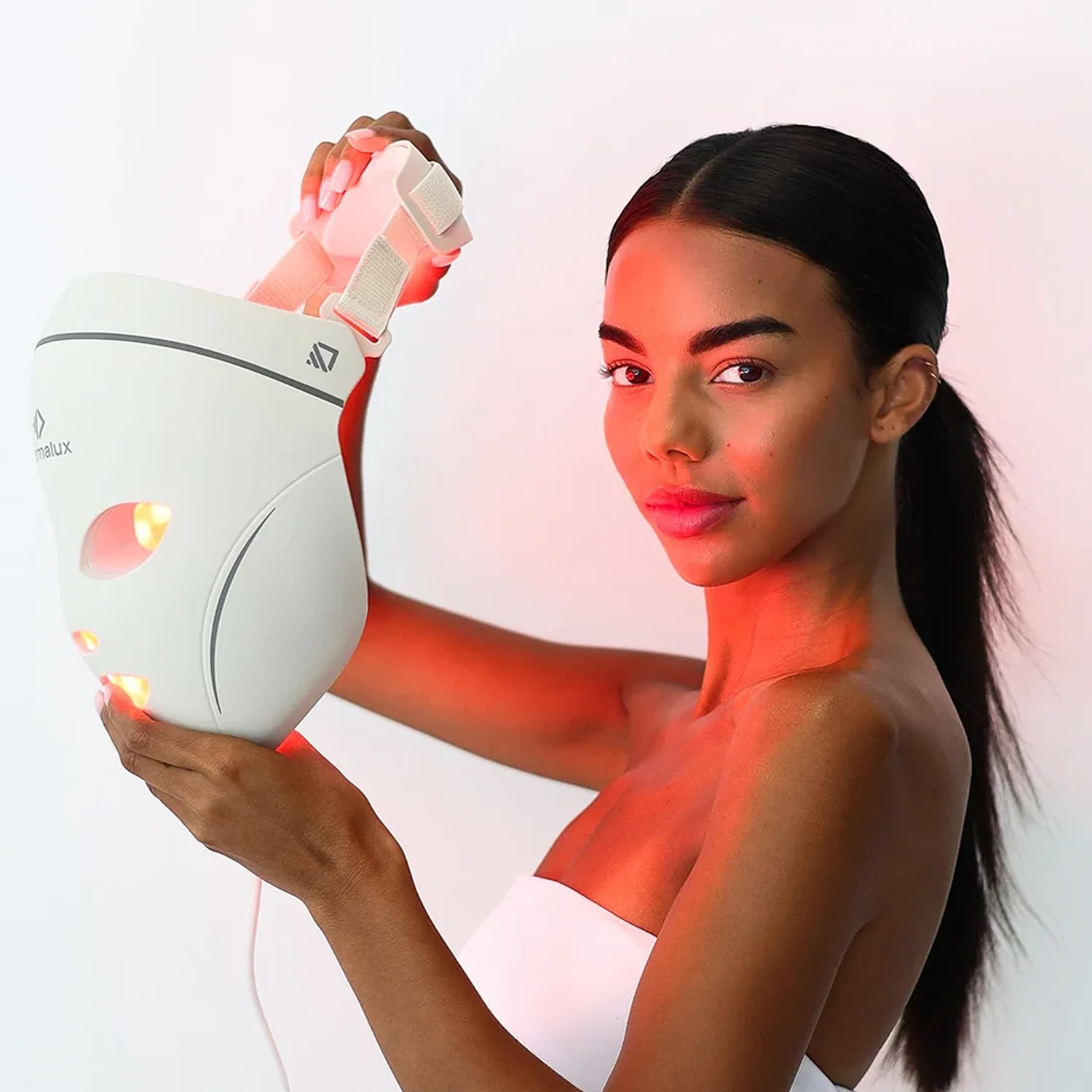 Model holding the lit Dermalux LED Face Mask next to her face