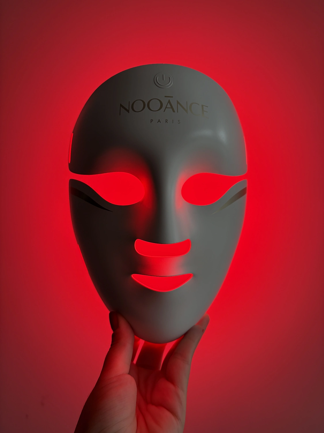 Front of the white Aurion X252 LED mask switched on, red light showing through the eye, nose and mouth cutouts